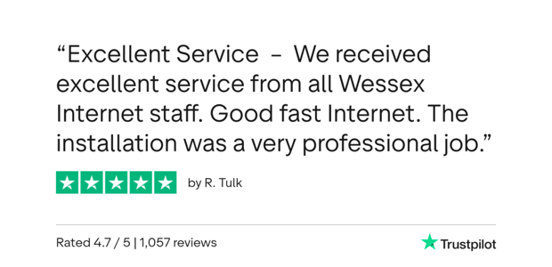 A woman sits at a laptop in her kitchen accessing the internet via her home broadband as her child watches on