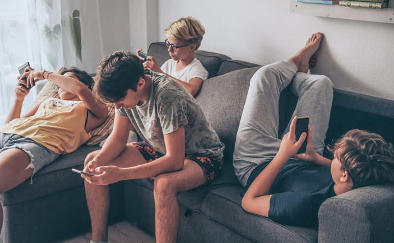 four teenagers lounging on a sofa all using a total wifi connection on various devices