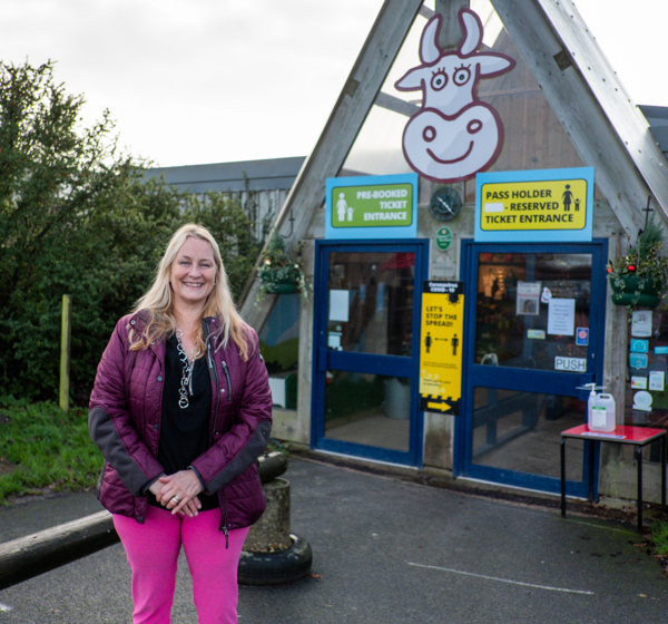 A lady stands smiling in front of Farmer Palmers entrance, in Poole, Dorset.